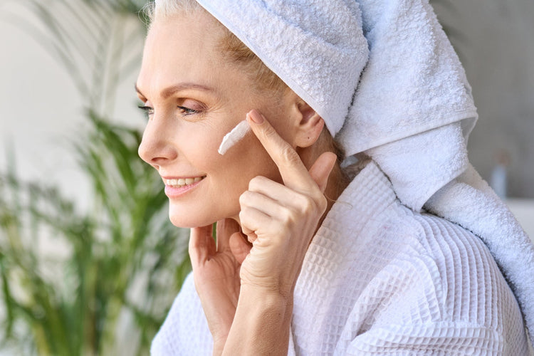 Woman in robe applying retinol anti-aging skincare product