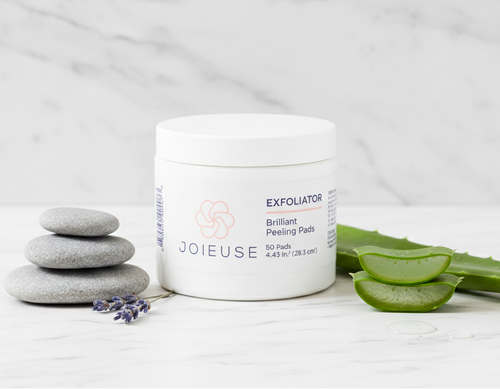 Joieuse exfoliator jar with peeling pads on a white surface with aloe vera and stones.